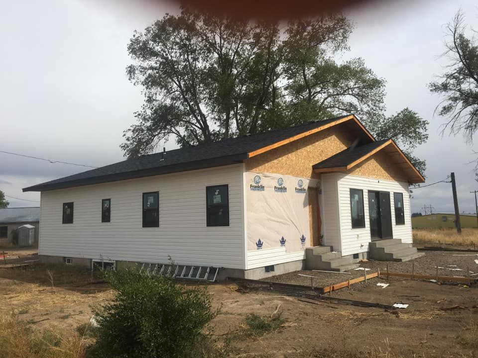 A white house with a black roof is sitting on top of a dirt field.