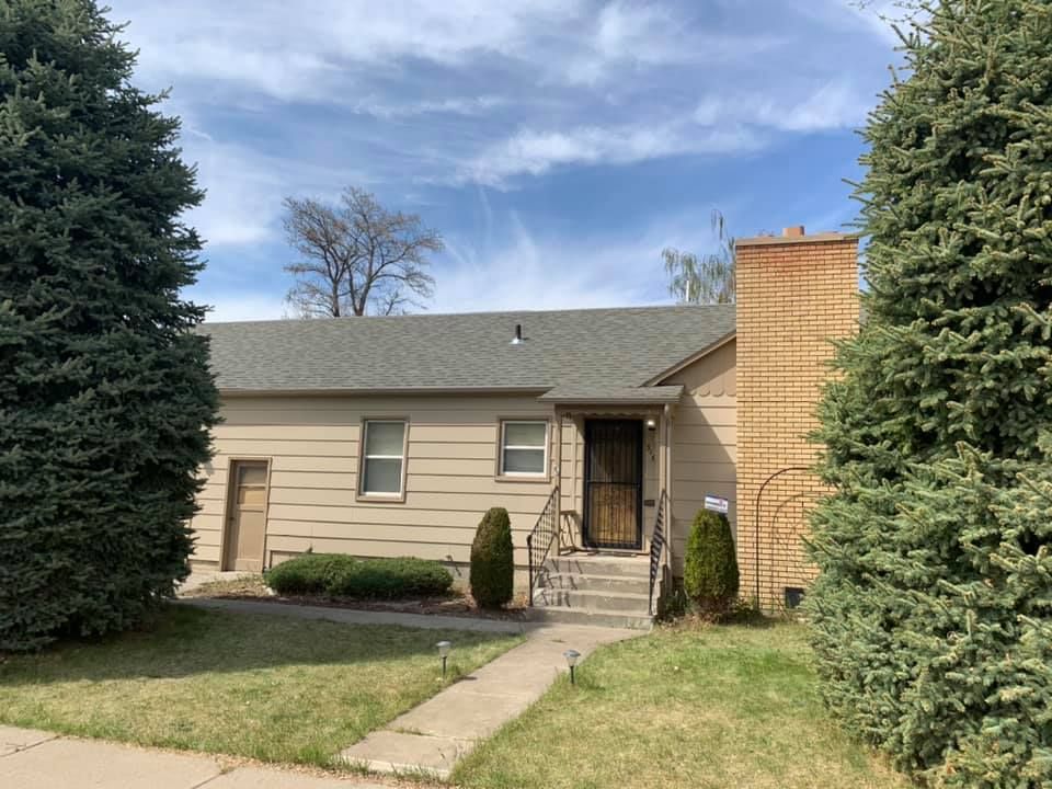 A house with a gray roof is surrounded by trees and bushes.