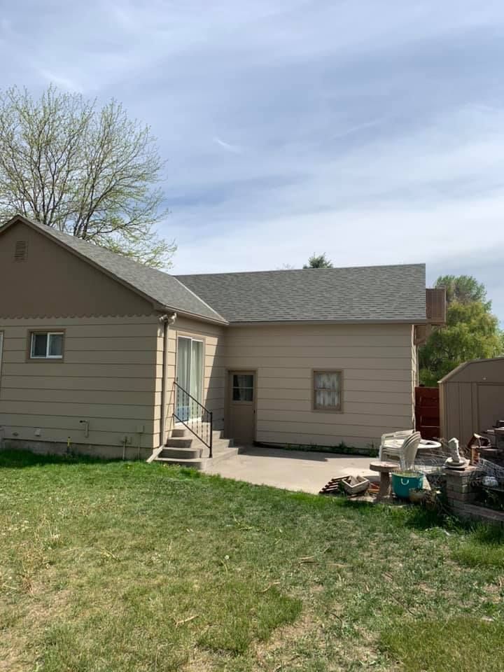 A house with a gray roof is sitting on top of a lush green field.