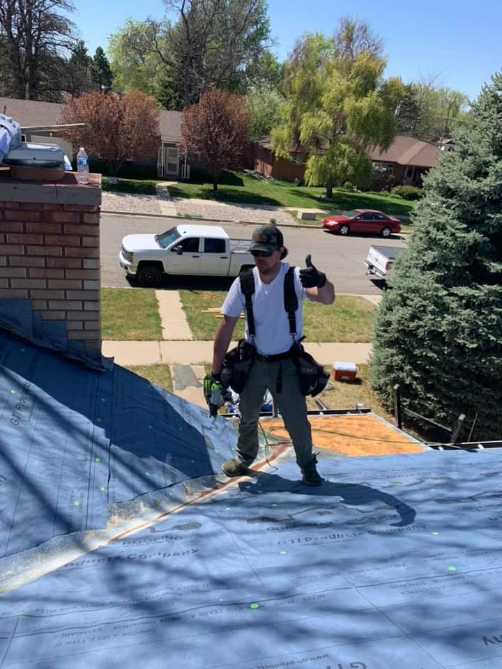 A man is standing on top of a roof giving a thumbs up.