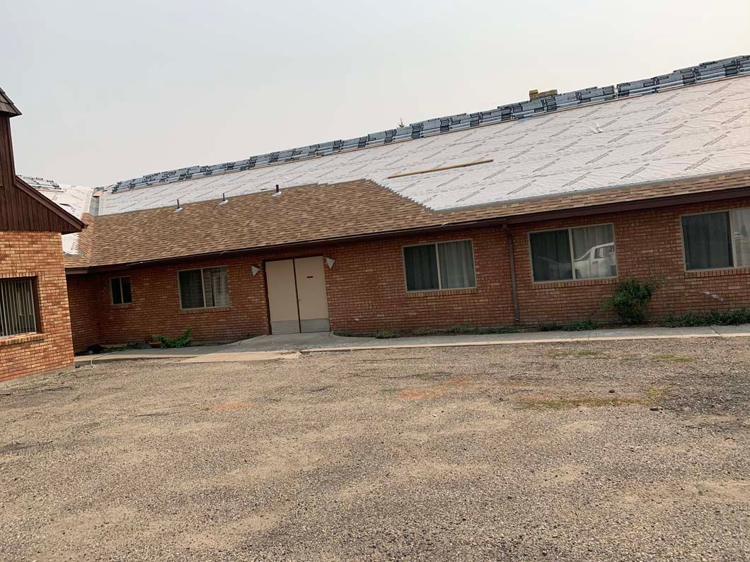 A large brick house with a tiled roof is sitting in the middle of a dirt field.