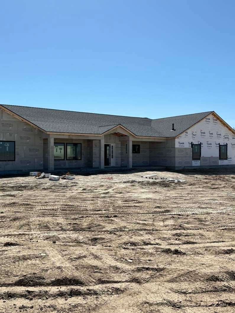 A large house is being built in the middle of a dirt field.