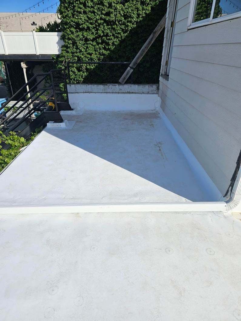 A white roof with a black railing on the side of a house.