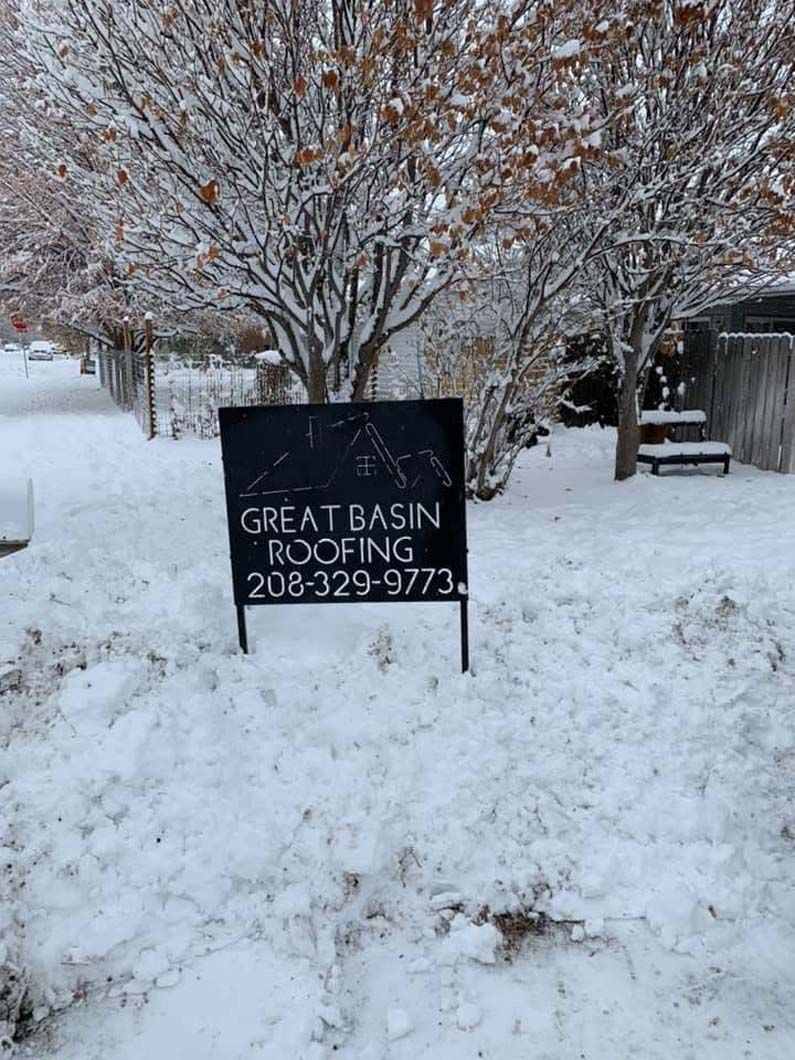 A sign for great basin roofing is sitting in the snow.