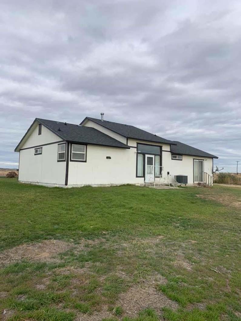 A white house with a black roof is sitting on top of a lush green field.