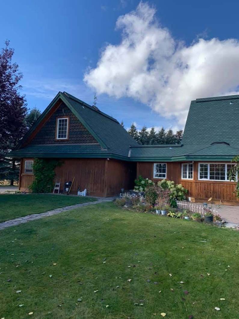 A large wooden house with a green roof and a large lawn in front of it.