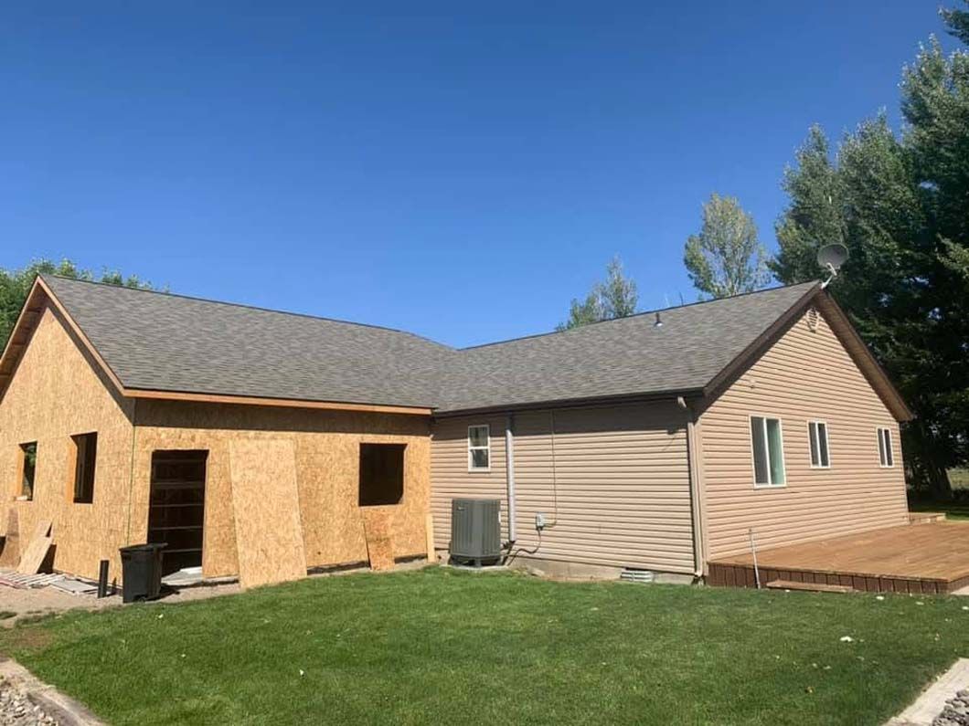 A house with a gray roof is being built in a backyard.
