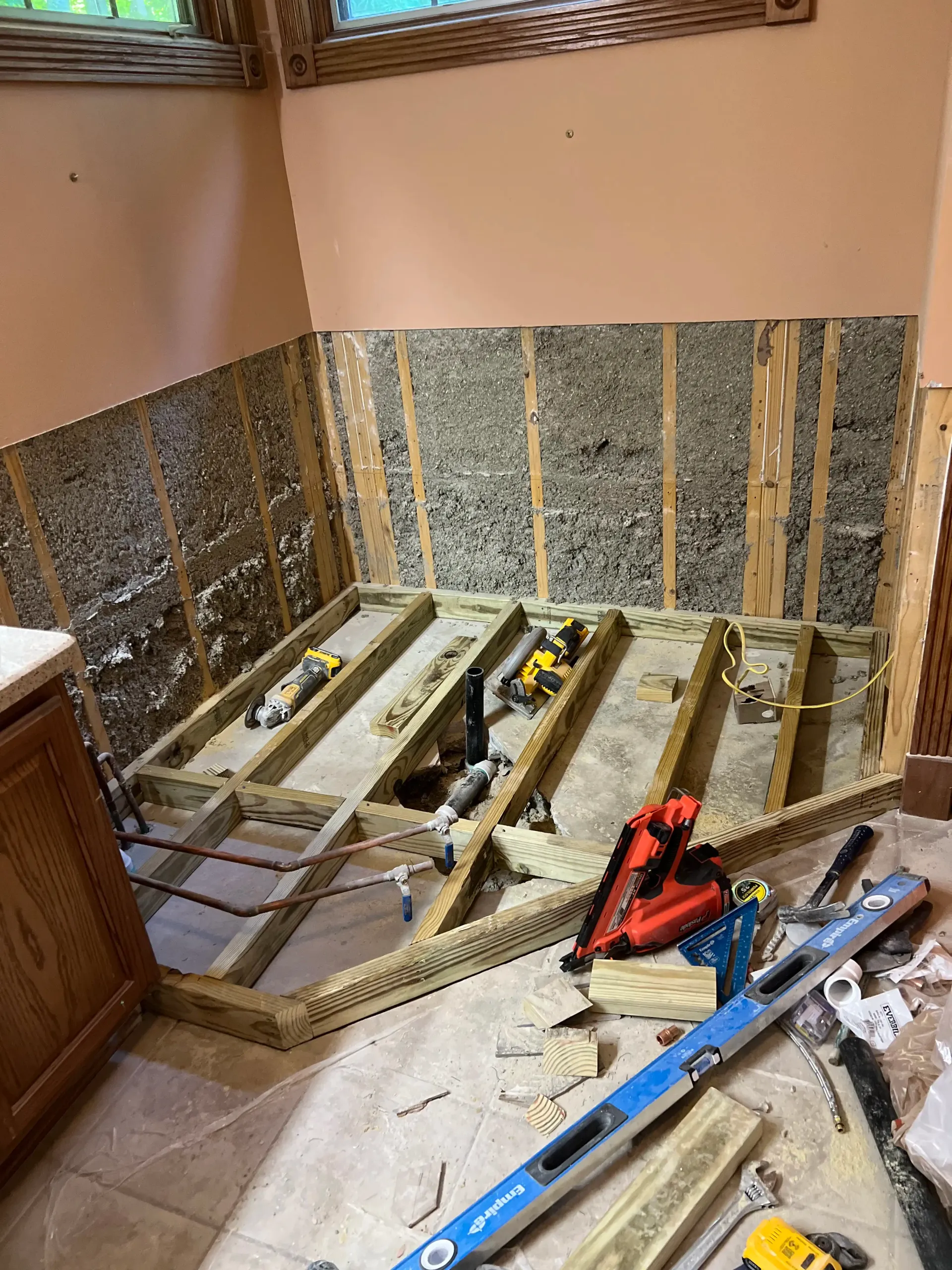 A bathroom renovation in progress, showing exposed wall studs and a newly framed wooden subfloor base for a tub.