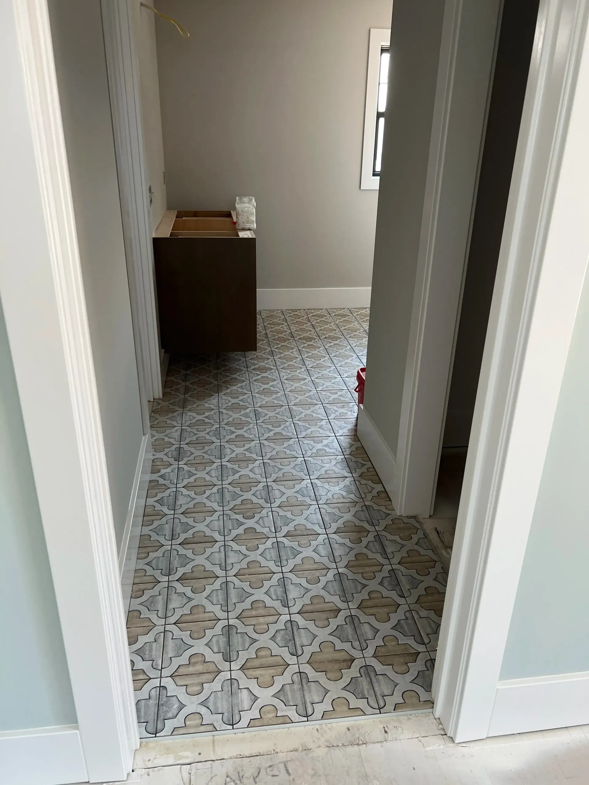 An empty garage with a grey speckled epoxy floor, light grey walls, and a white door with wooden stairs.