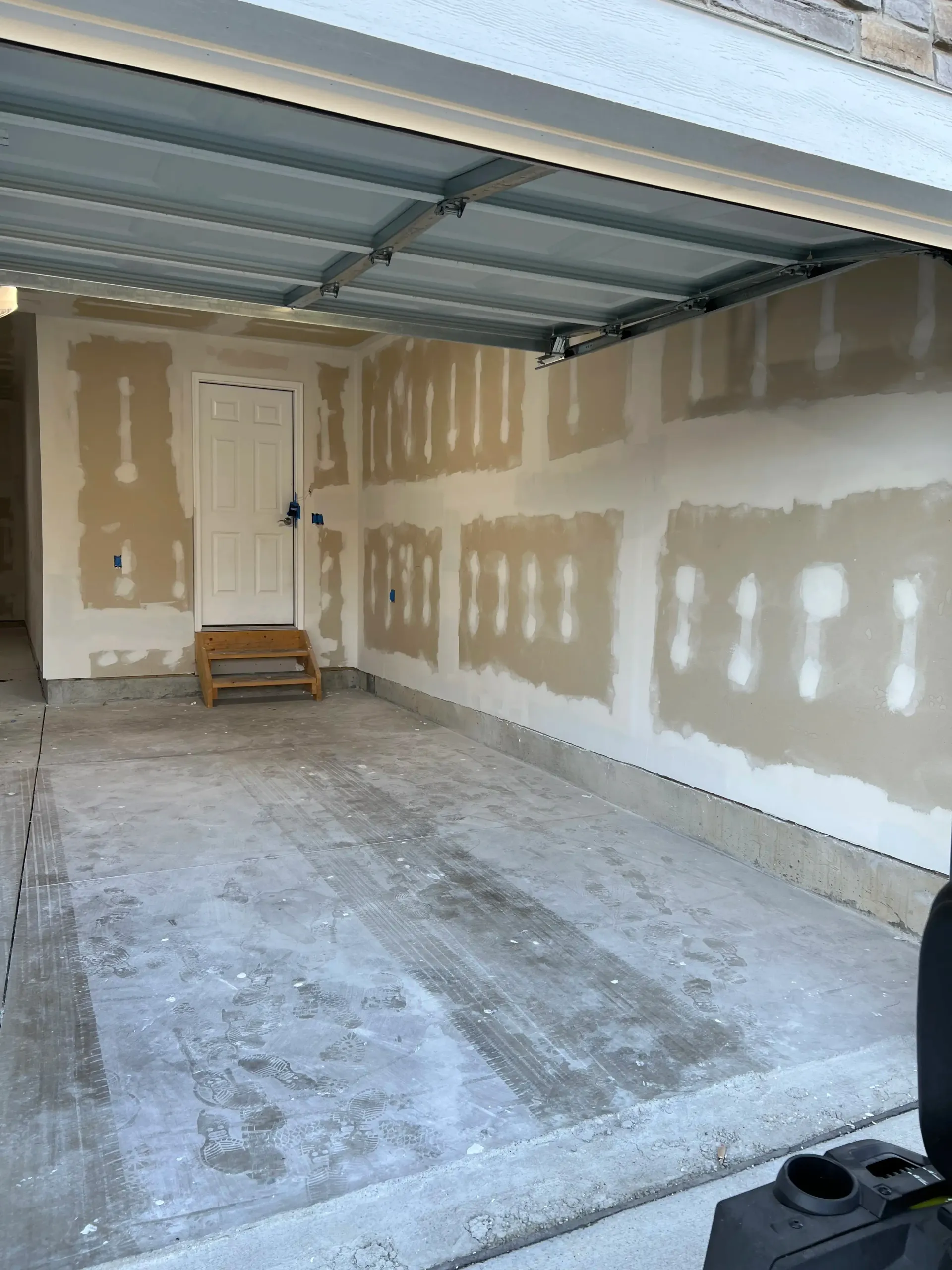 A garage interior with unfinished drywall showing taped seams and a white door with a small step stool in front.