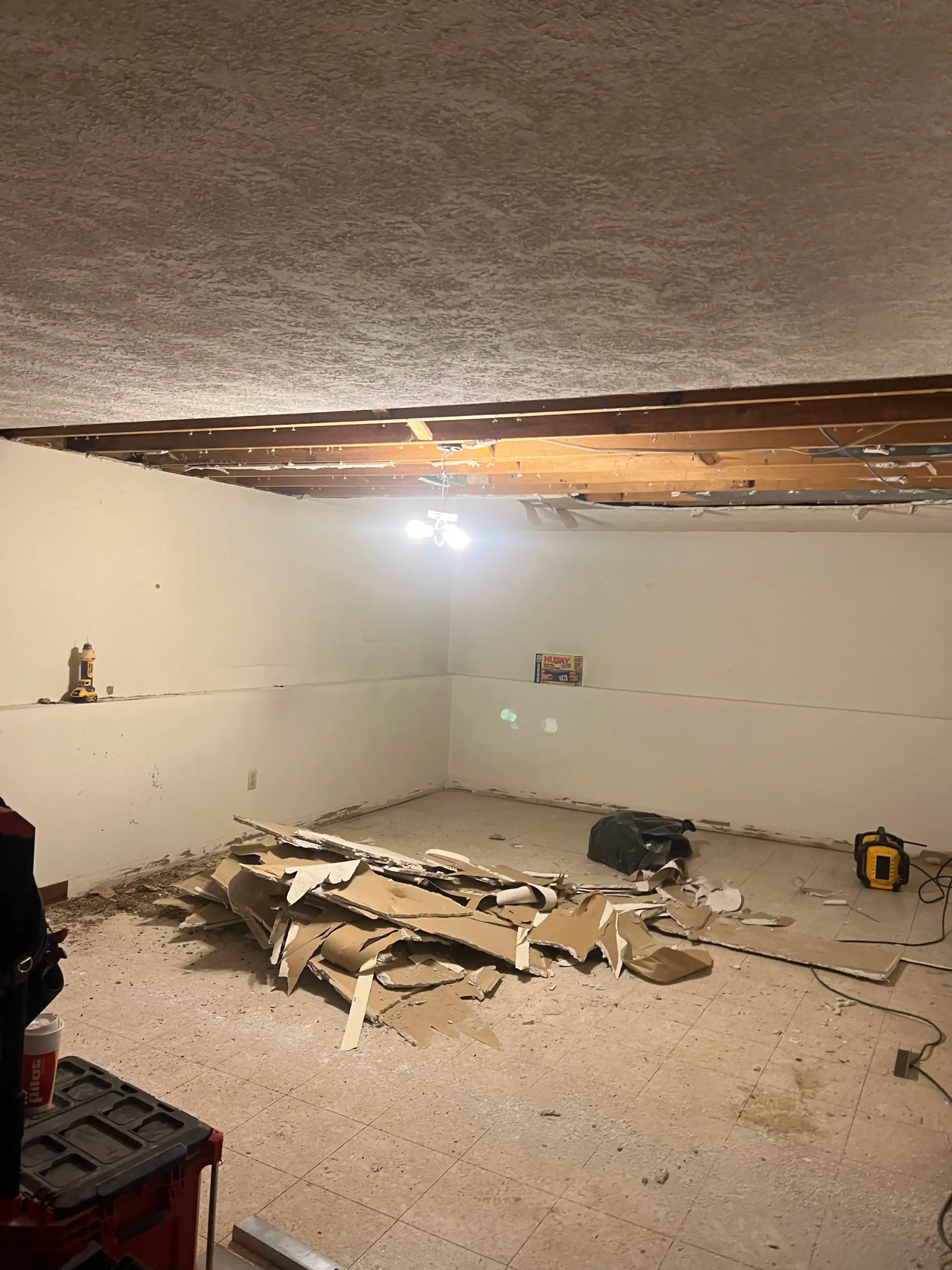 An interior room undergoing renovation with exposed wooden ceiling joists and piles of debris on the floor.