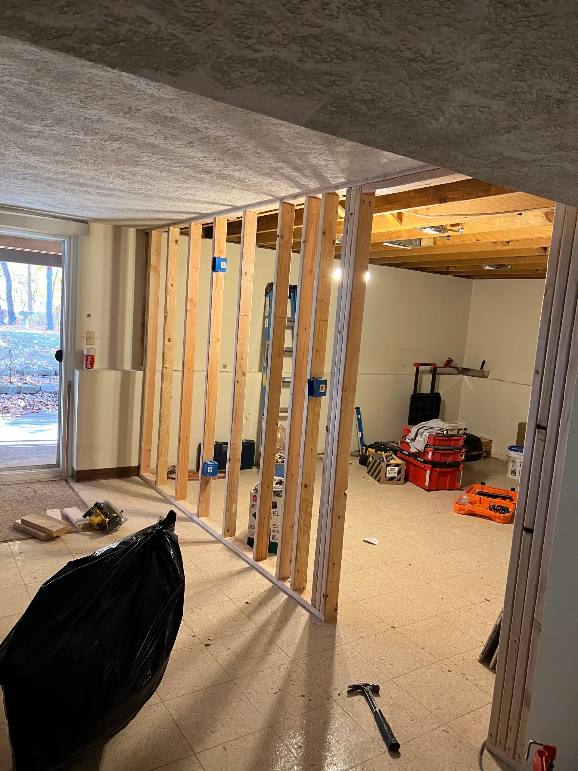 A wooden stud wall partition under construction in a basement, with electrical boxes visible in the frame.