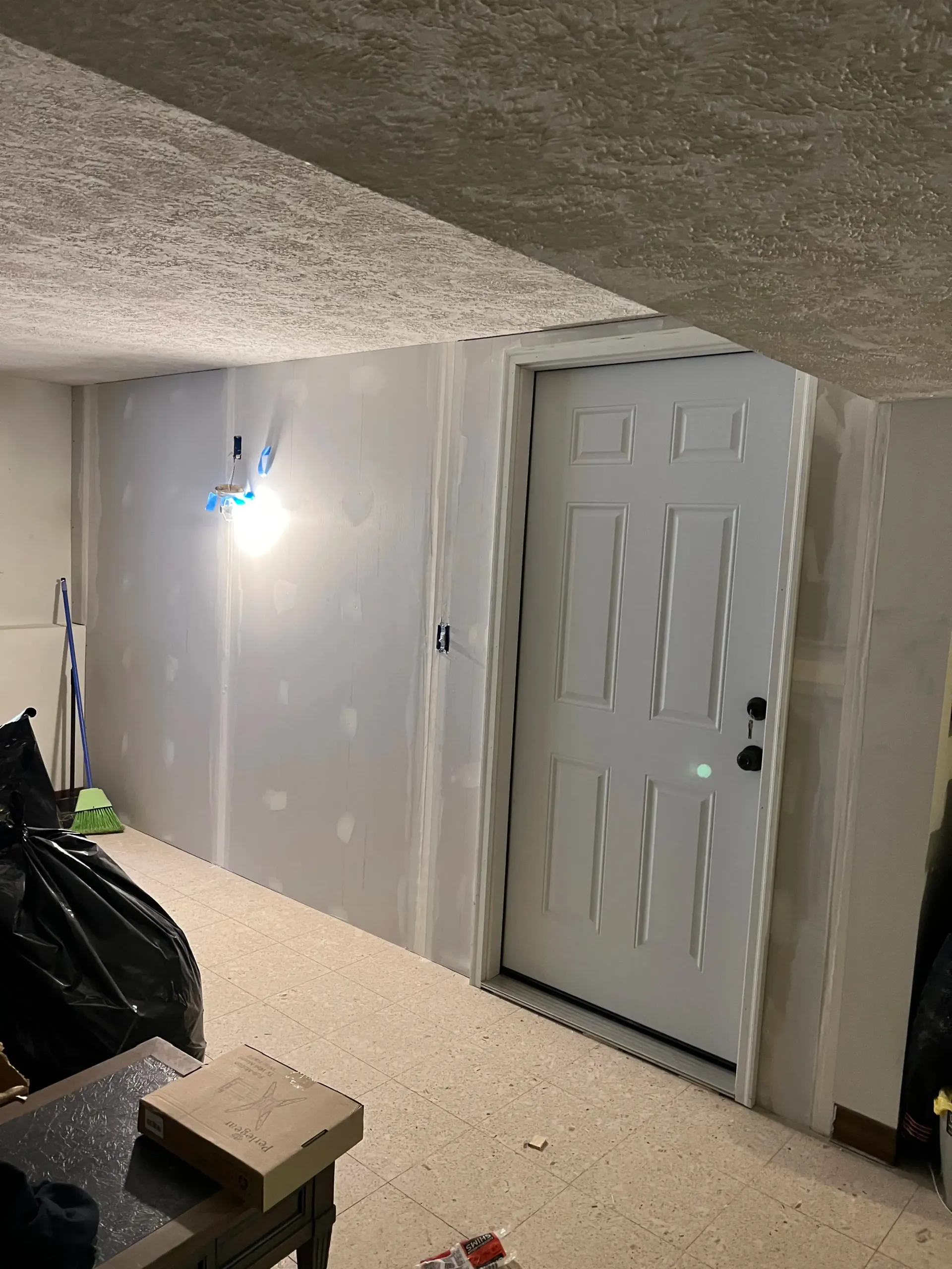 A white interior door set in a wall with unfinished drywall seams, situated in a basement room with a textured ceiling.