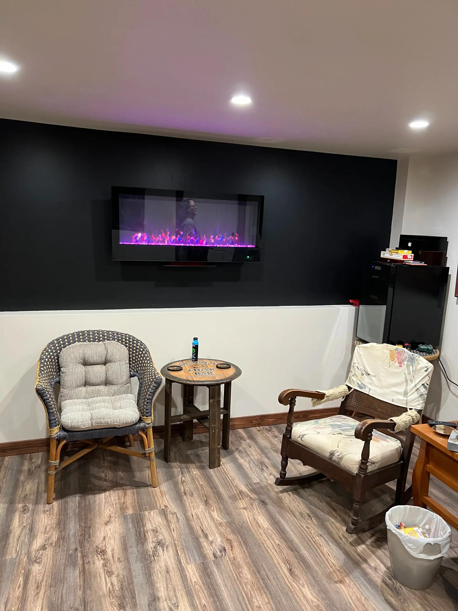 A lounge area with two chairs, a side table, and a wall-mounted electric fireplace against a black and white wall.