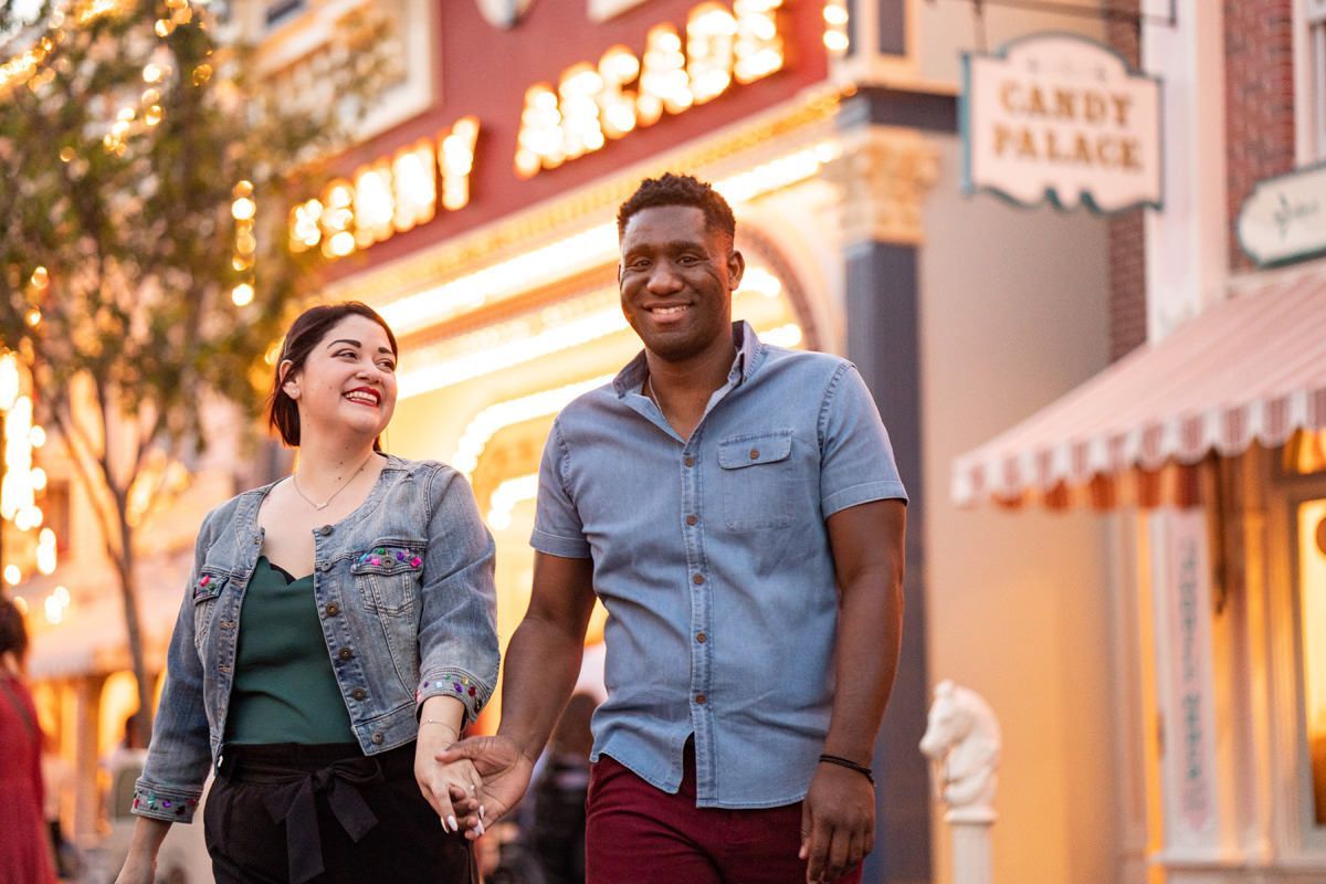 A man and a woman are walking down Main street in Disneyland holding hands.