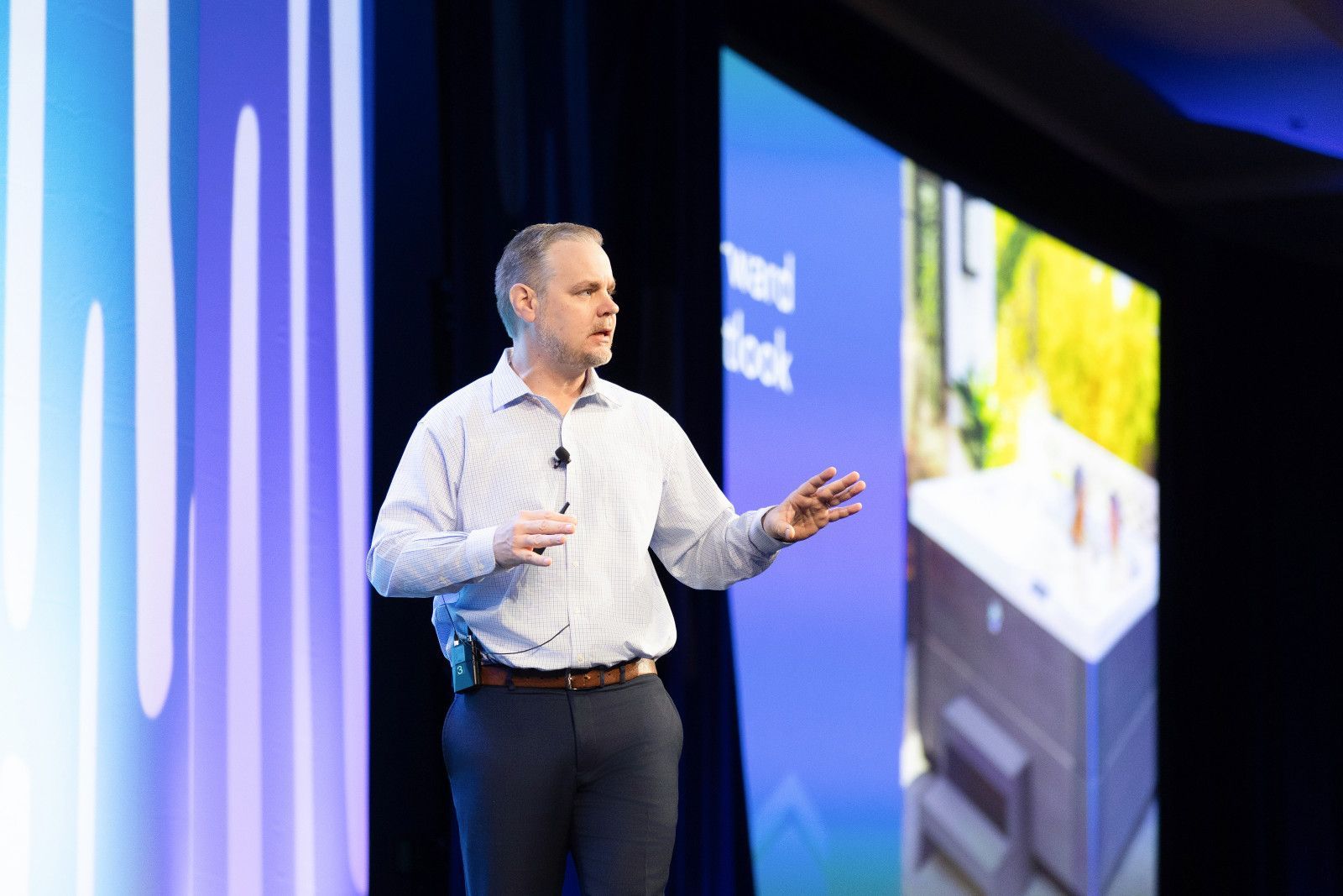 planning orange county conference photo A person in a dress shirt and trousers stands on stage, gesturing while presenting in front of a blue display screen at conference in Orange County