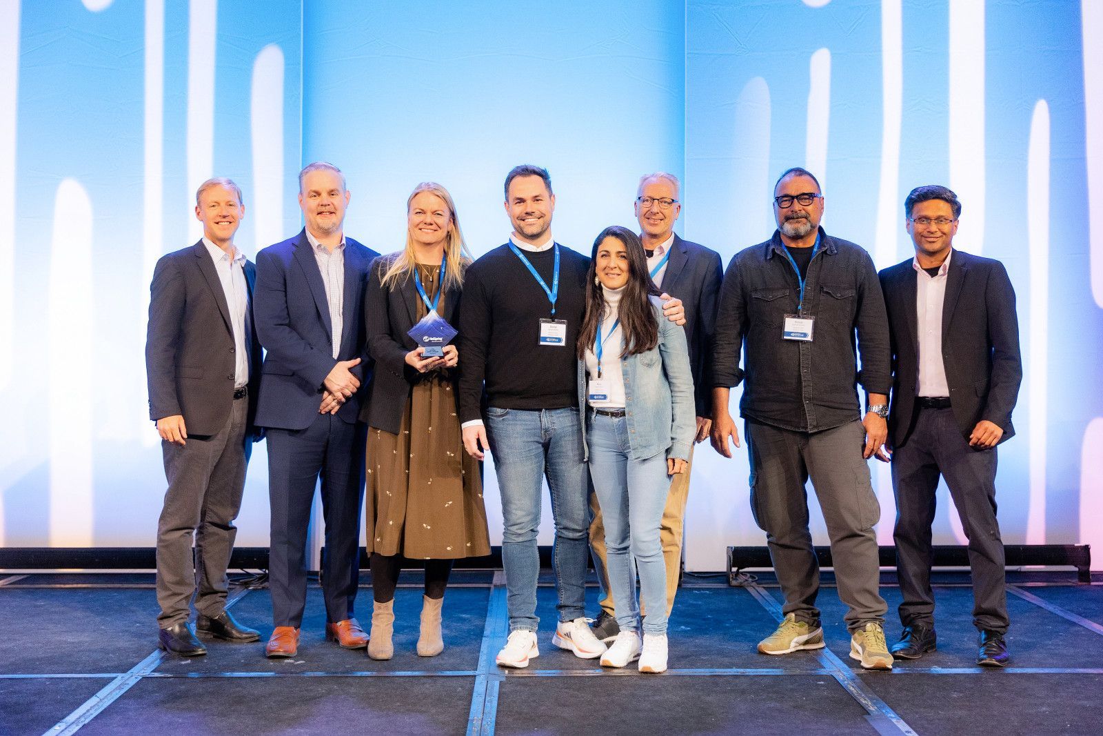 Orange County corporate event photography A group of eight people stand on a stage with a blue background, smiling as they hold an award during a conference.
