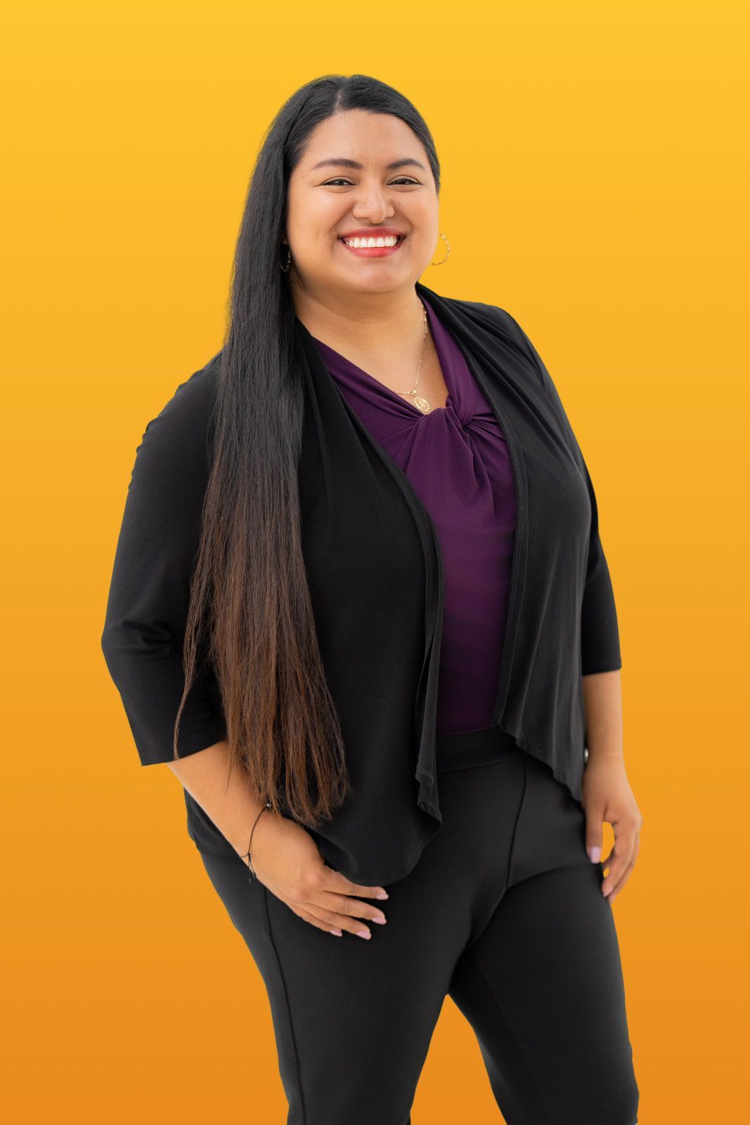 Orange County corporate headshots on-site session Woman smiling, wearing black blazer over purple top, black pants, long dark hair, against yellow background in Costa Mesa
