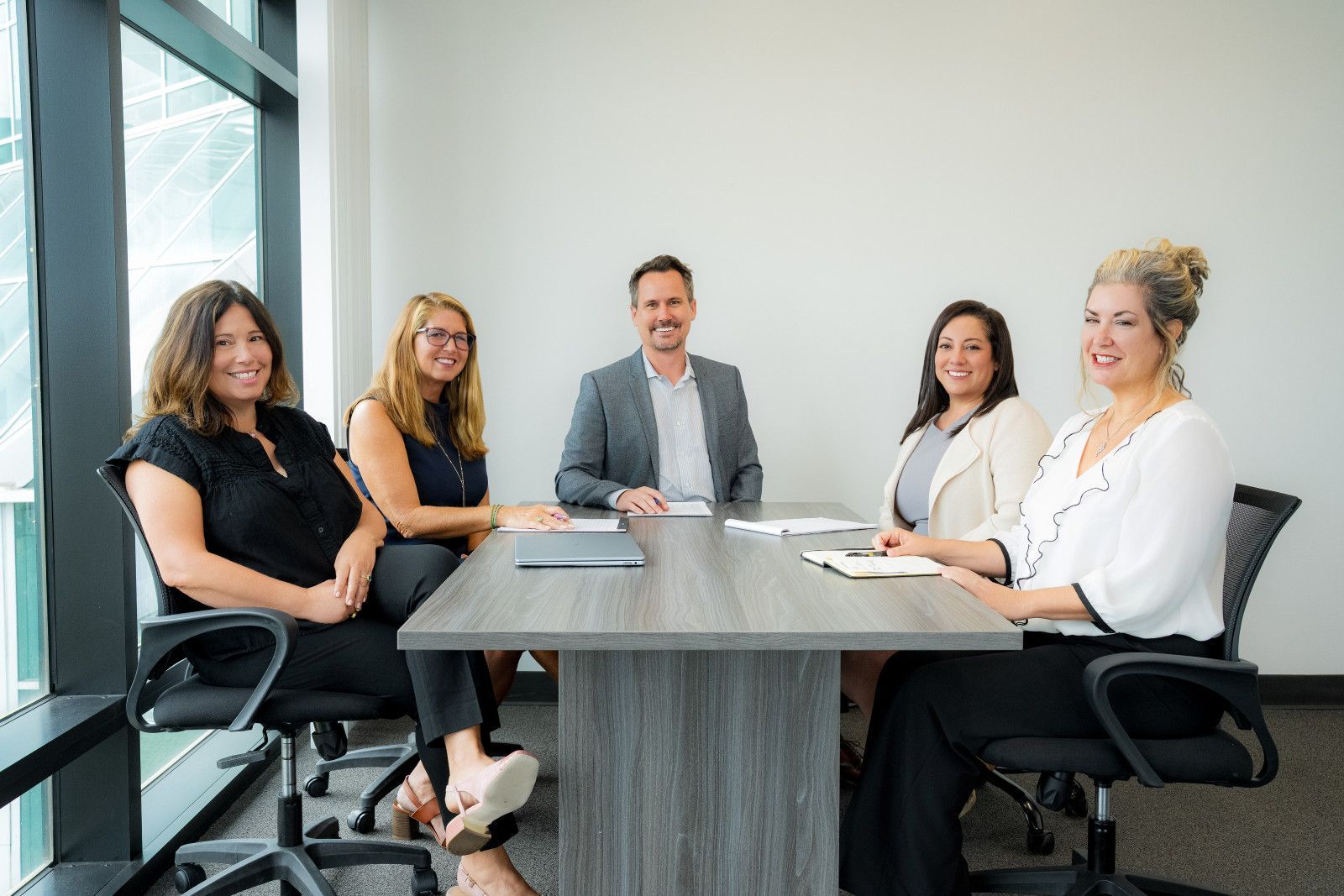 Five people seated around a table in an office, smiling in office in Orange County