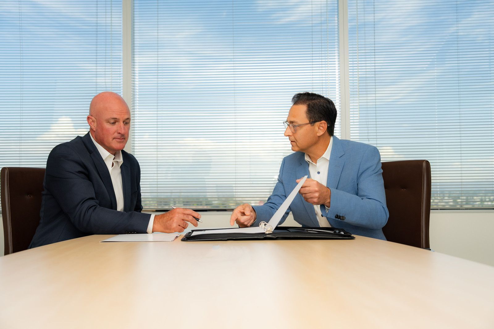 Two men at a table reviewing documents in a well-lit office. One points, the other writes.
