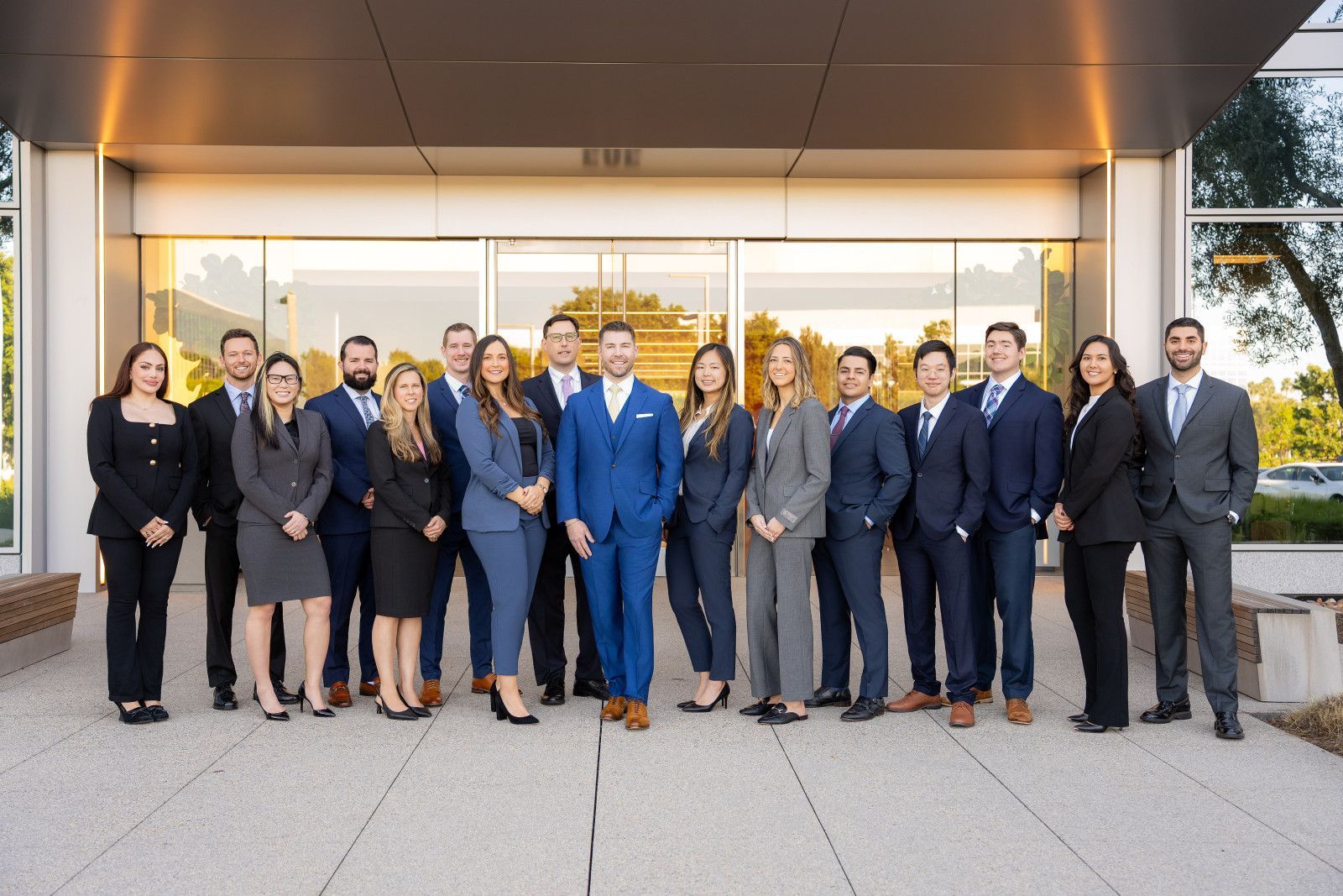orange County Law Firm A law firm group in business attire stands in two rows outside a building entrance, posing for a portrait.