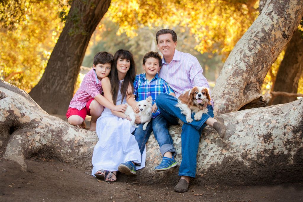 A family is sitting on a tree branch with their dogs in Irvine regional Park.