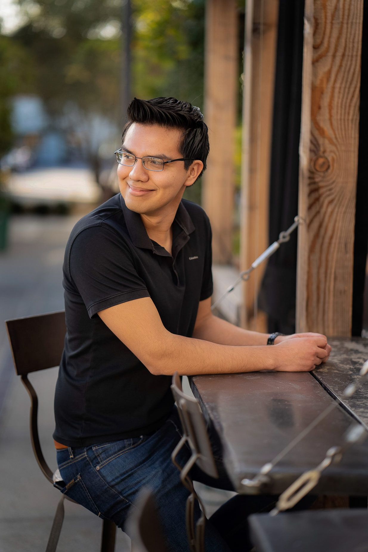 A young man wearing glasses is sitting at a table for dating app photos.