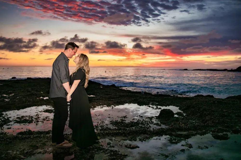 A man and a woman are kissing on the beach at sunset.