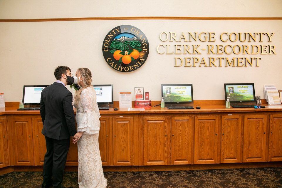 A bride and groom are kissing in front of the orange county clerk recorder department.