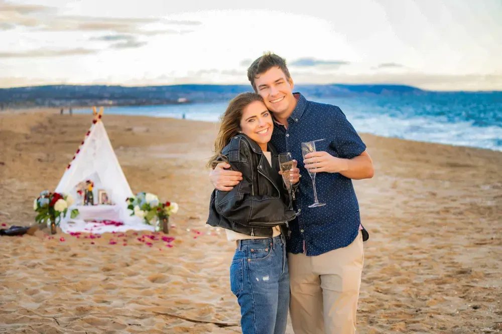 A couple standing on a beach holding champagne glasses.