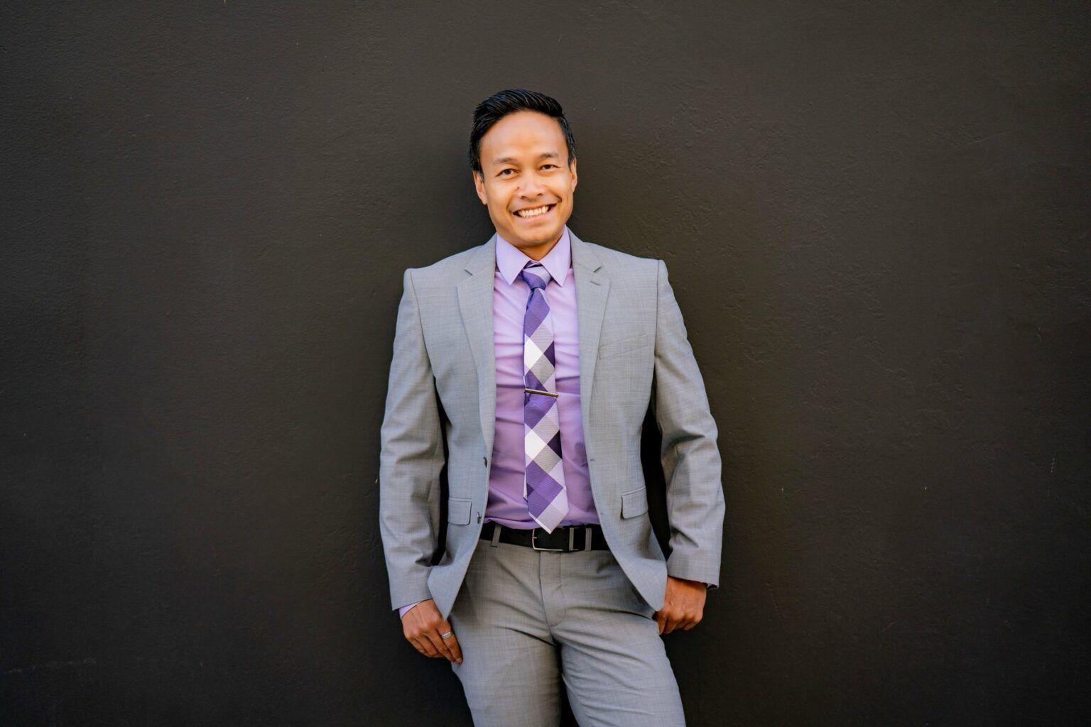 A man in a suit and tie is standing in front of a black wall.