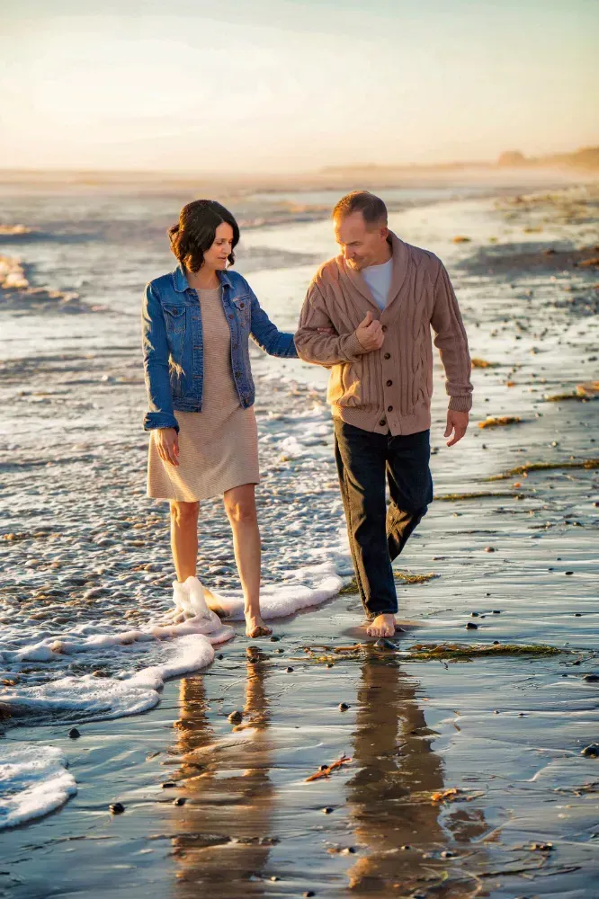 A man and a woman are walking on the beach during low tide and sunset.