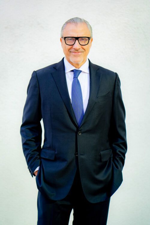 Professional headshot with A man in a suit and tie with his hands in his pockets