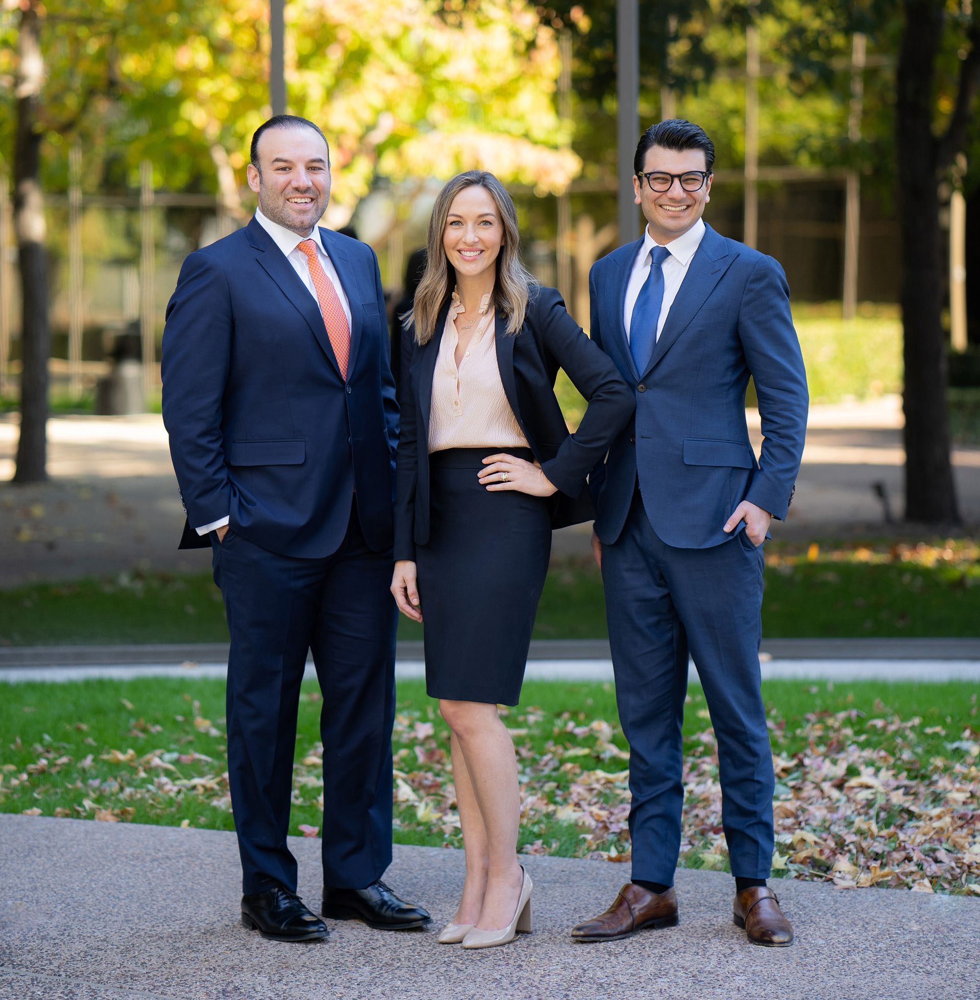 Three people in suits and ties are posing for professional shots.