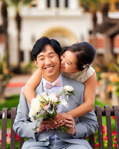A bride and groom are posing for a picture while sitting on a bench.