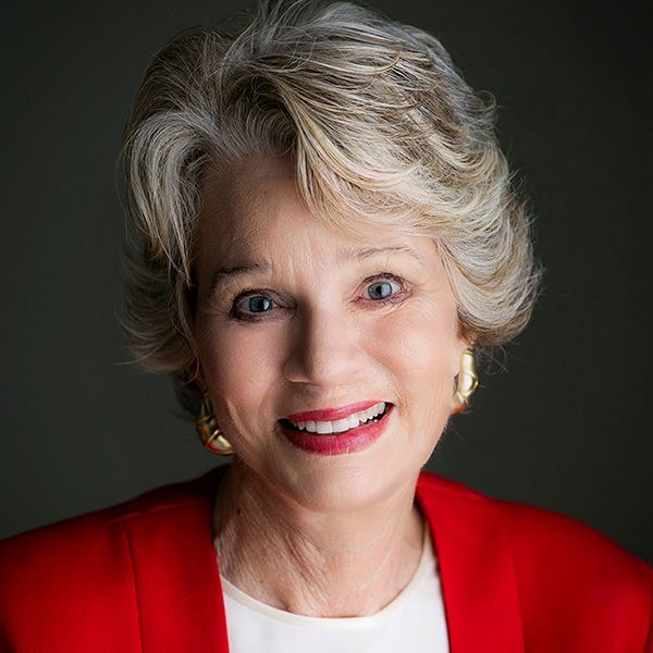 A woman wearing a red jacket and earrings is smiling for the camera.