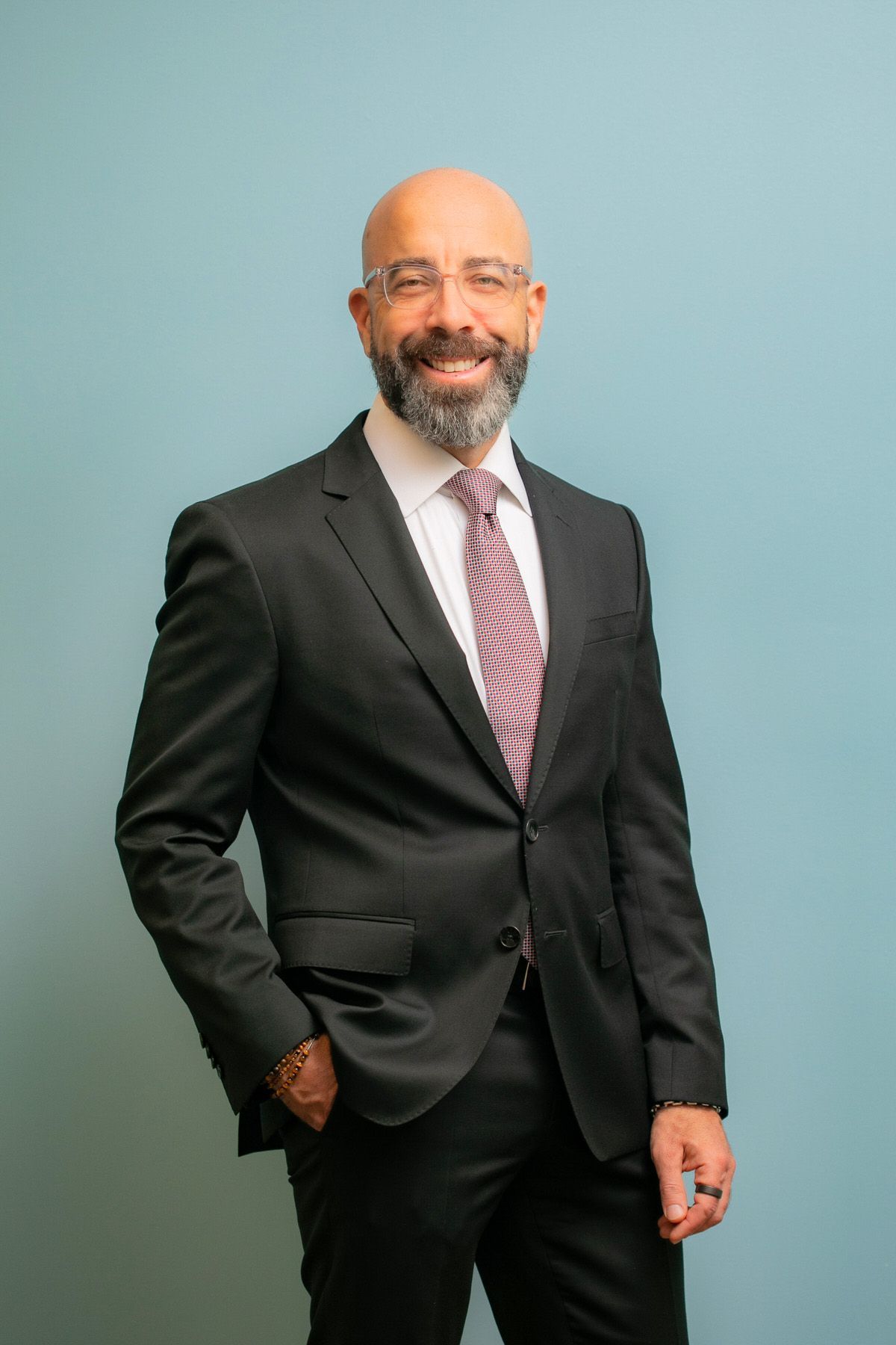 An attorney in a suit and tie is standing with his hands in his pockets for a headshot