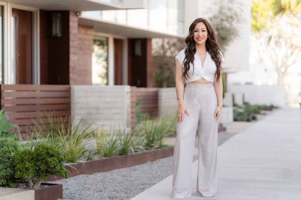 A woman is standing on a sidewalk in front of a building.