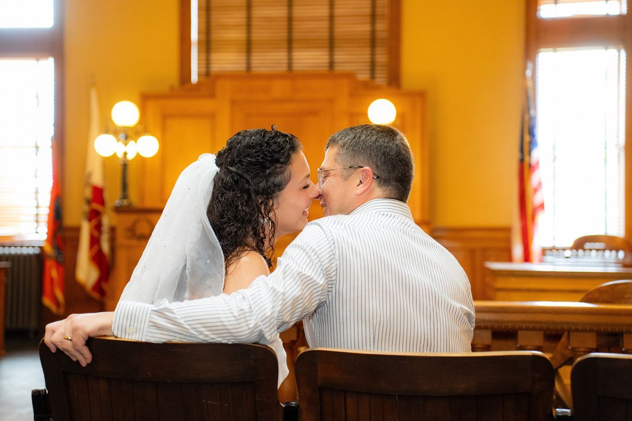 A bride and groom are kissing while sitting in the historic courtroom in santa ana