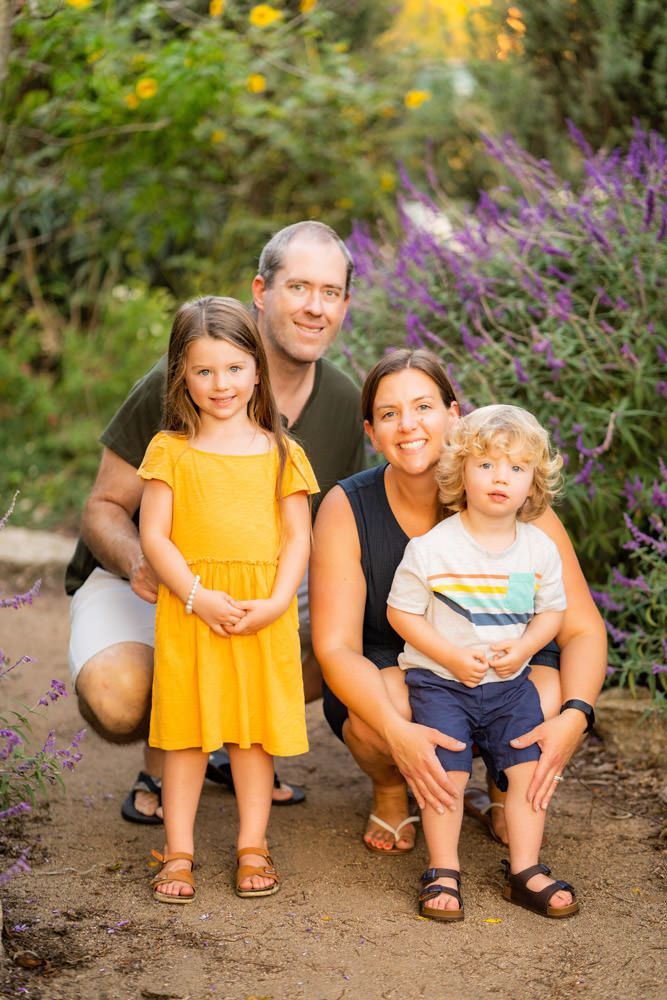 Family Portraits In Park A family is posing for a picture in front of purple flowers.