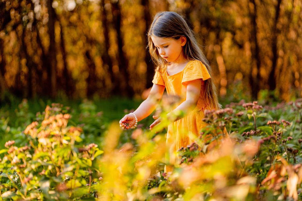 A little girl in a yellow dress is standing in a field of flowers.