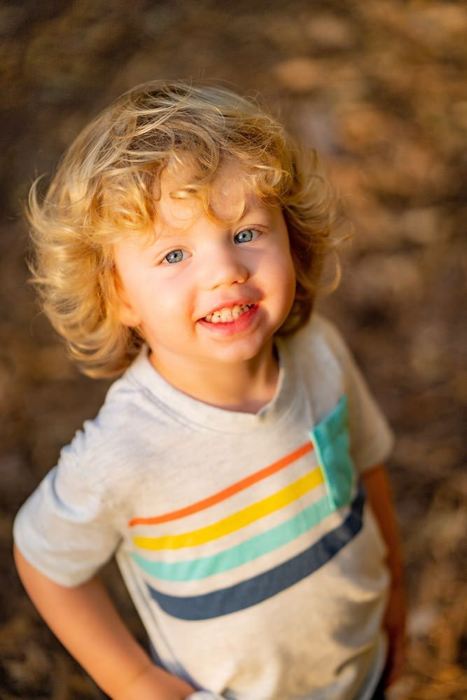 A young boy with blonde hair and blue eyes is wearing a striped t-shirt and smiling.