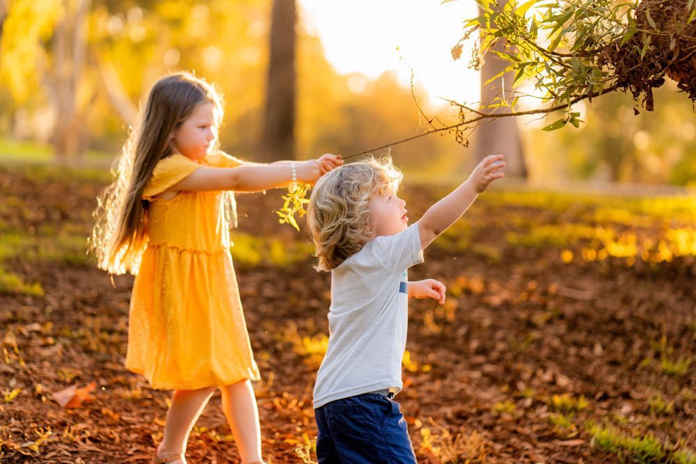 A boy and a girl are playing with leaves in a park.