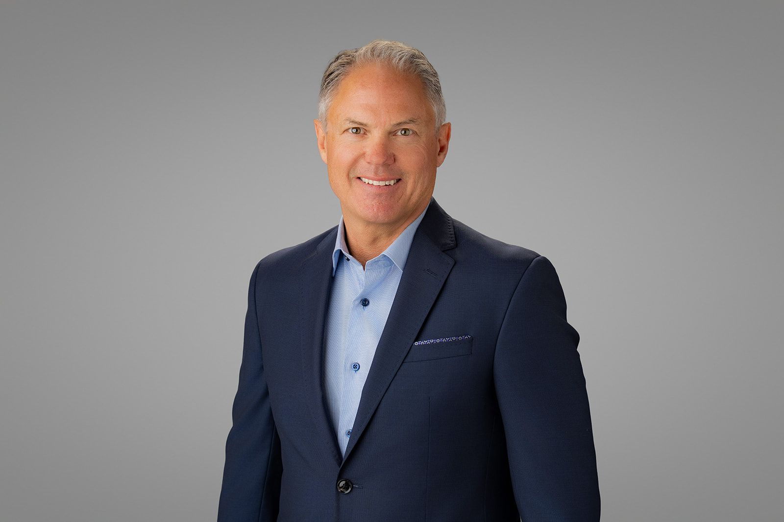 Man in blue shirt and blazer smiling against a gray background in newport beach ca