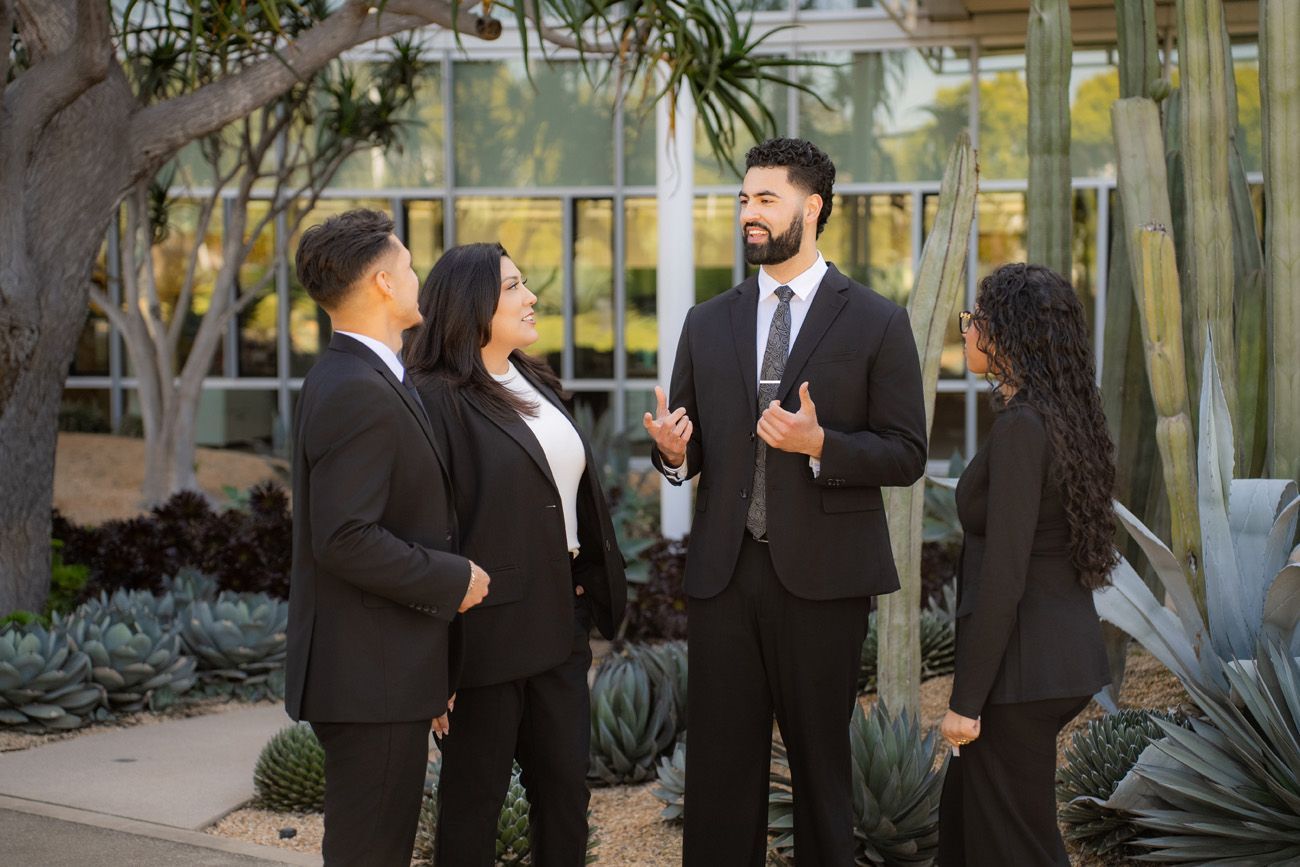 orange county law firm photography Four attorneys in business suits stand outdoors, engaged in a discussion among desert plants and a building in Newport Beach.