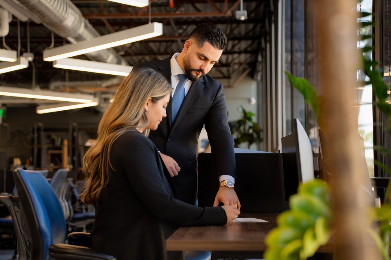 professional lawyer headshots day A male attorney in a suit stands by a desk, reviewing a document with someone seated at a computer in a modern office in Irvine