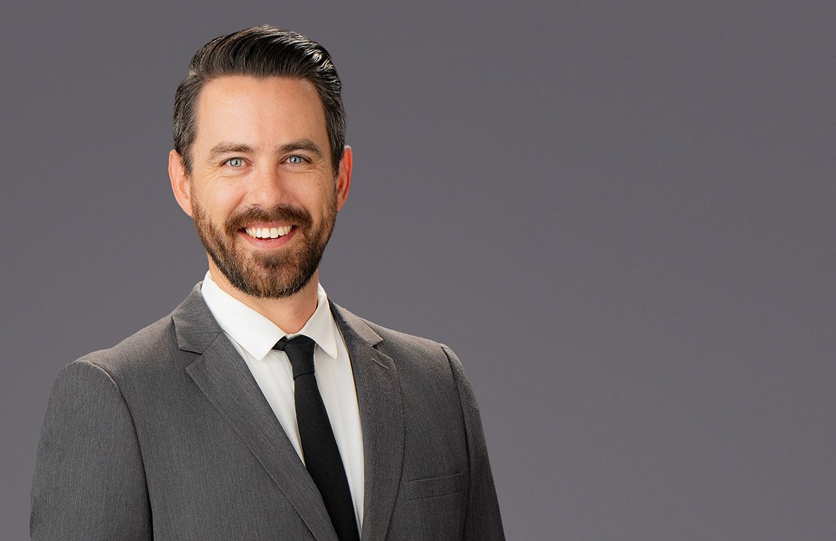 Male Corporate Team Headshots Irvine Man in gray suit and tie smiles against a gray background.