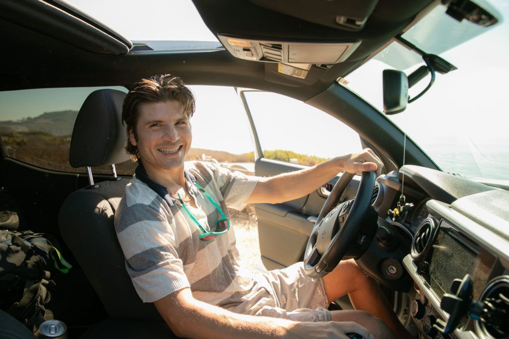A man is sitting in the driver's seat of a car for a dating app photo