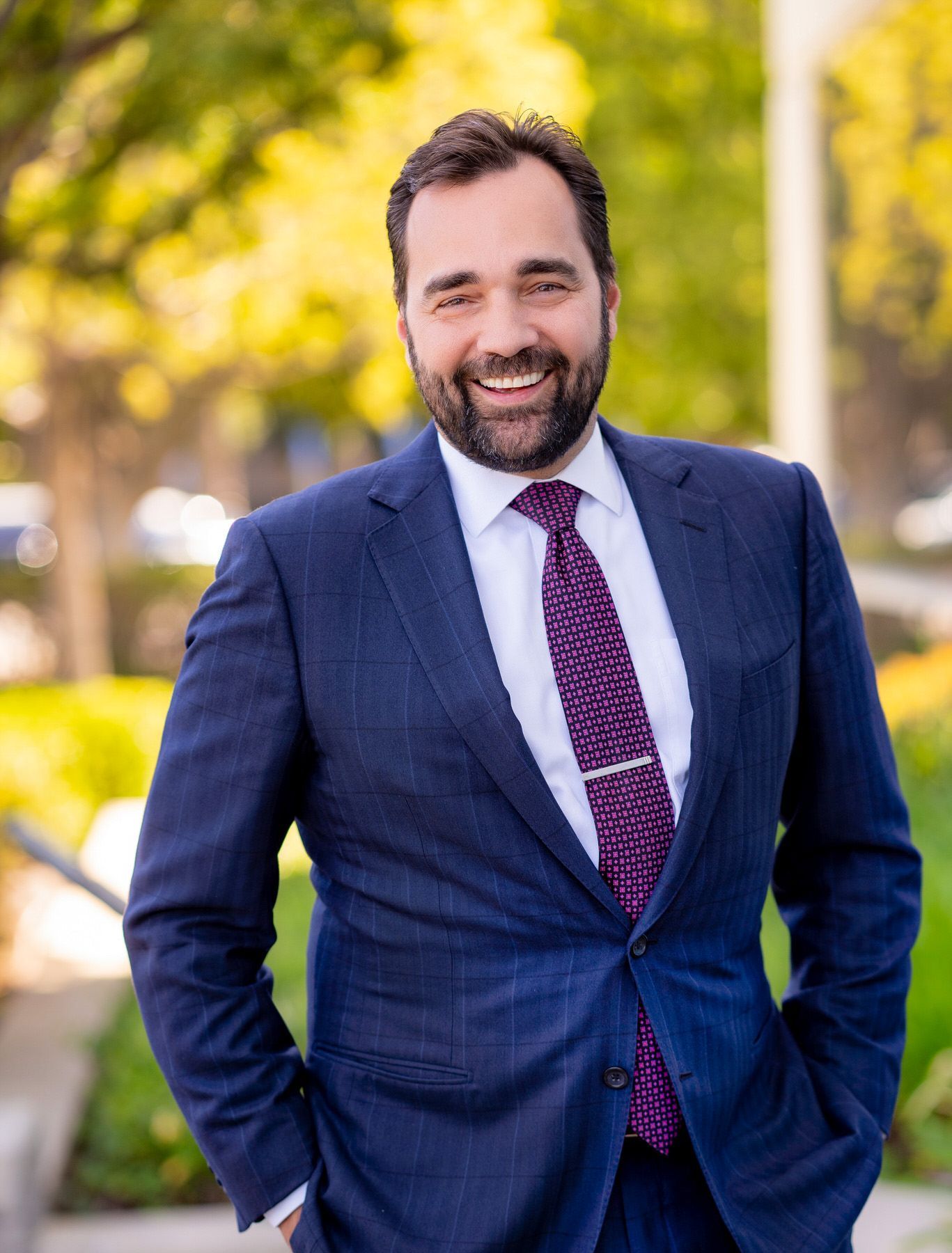 An attorney in a suit and tie is standing with his hands in his pockets.