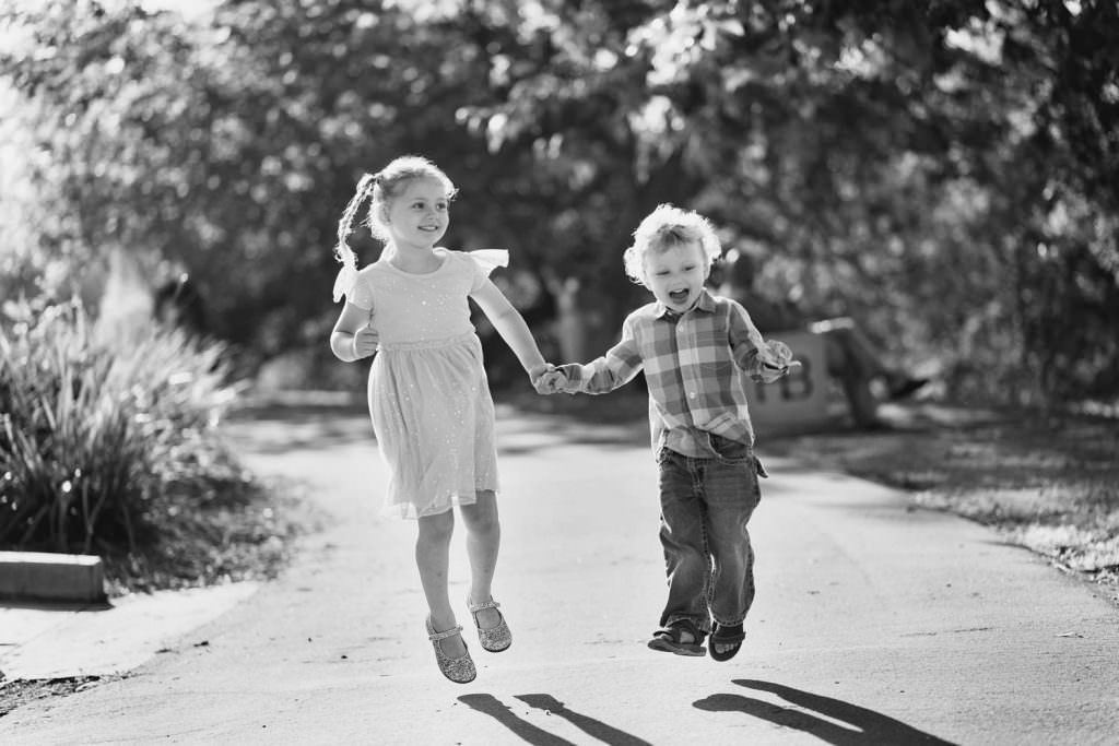 A boy and a girl are jumping in the air while holding hands, a candid black and white family photo.